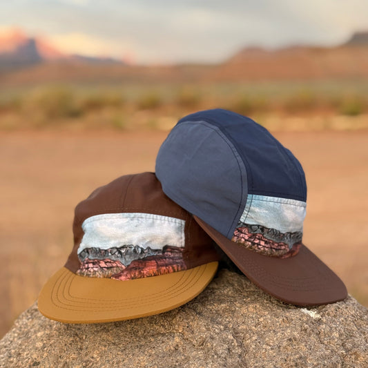 Two hats with desert landscape designs on a rock with a desert background